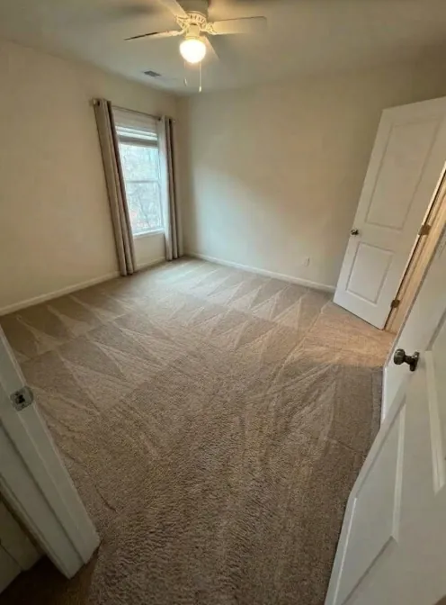 Empty bedroom with tan carpet and a ceiling fan