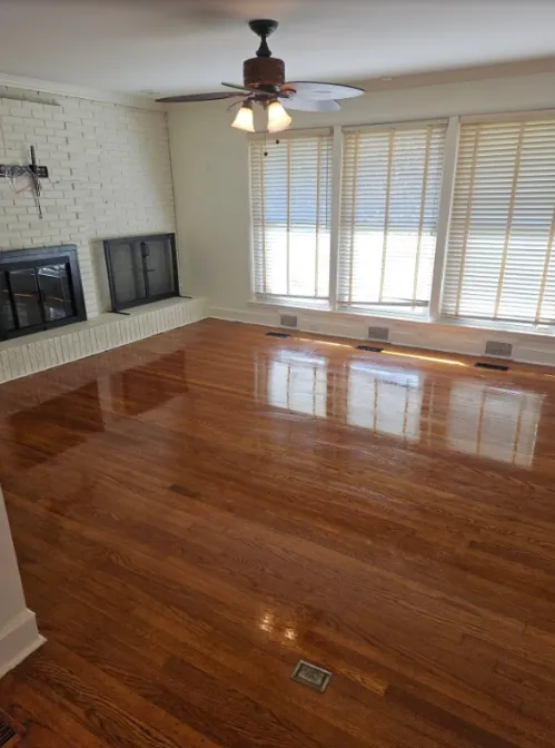 Polished hardwood floor in an empty room with a brick fireplace