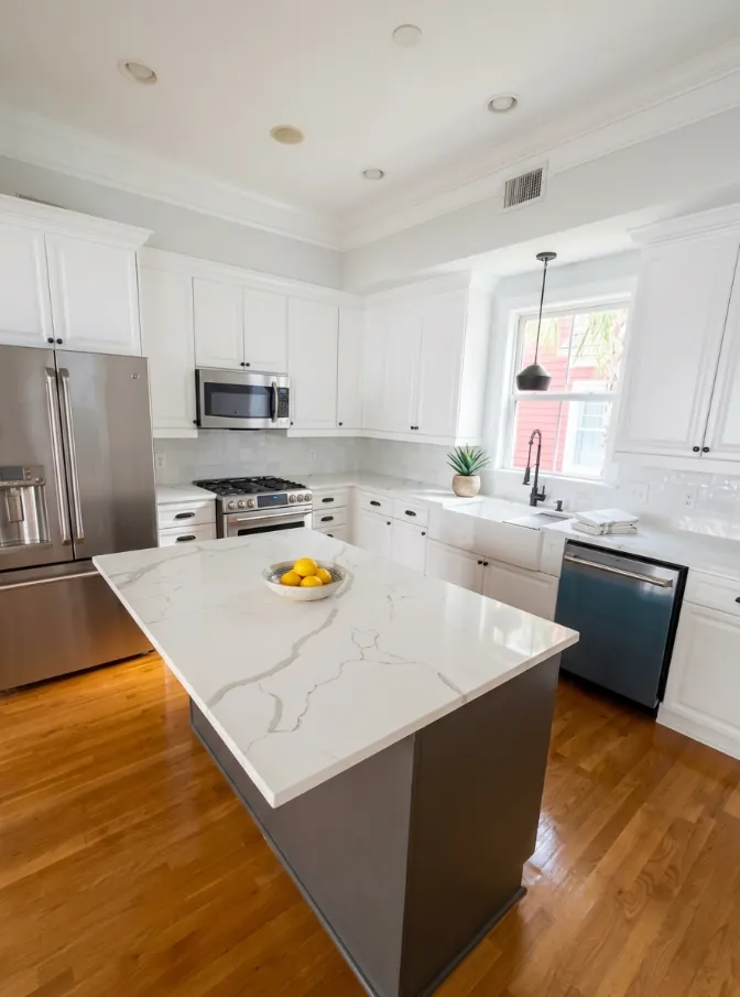 White kitchen with a marble-look island and hardwood floors